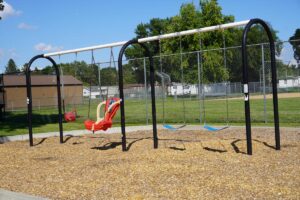 swing set at 16th St. Park with a brown building in the background