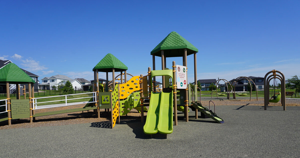 green, yellow, tan, and white playground at Elk Ridge Park with swing sets in the background