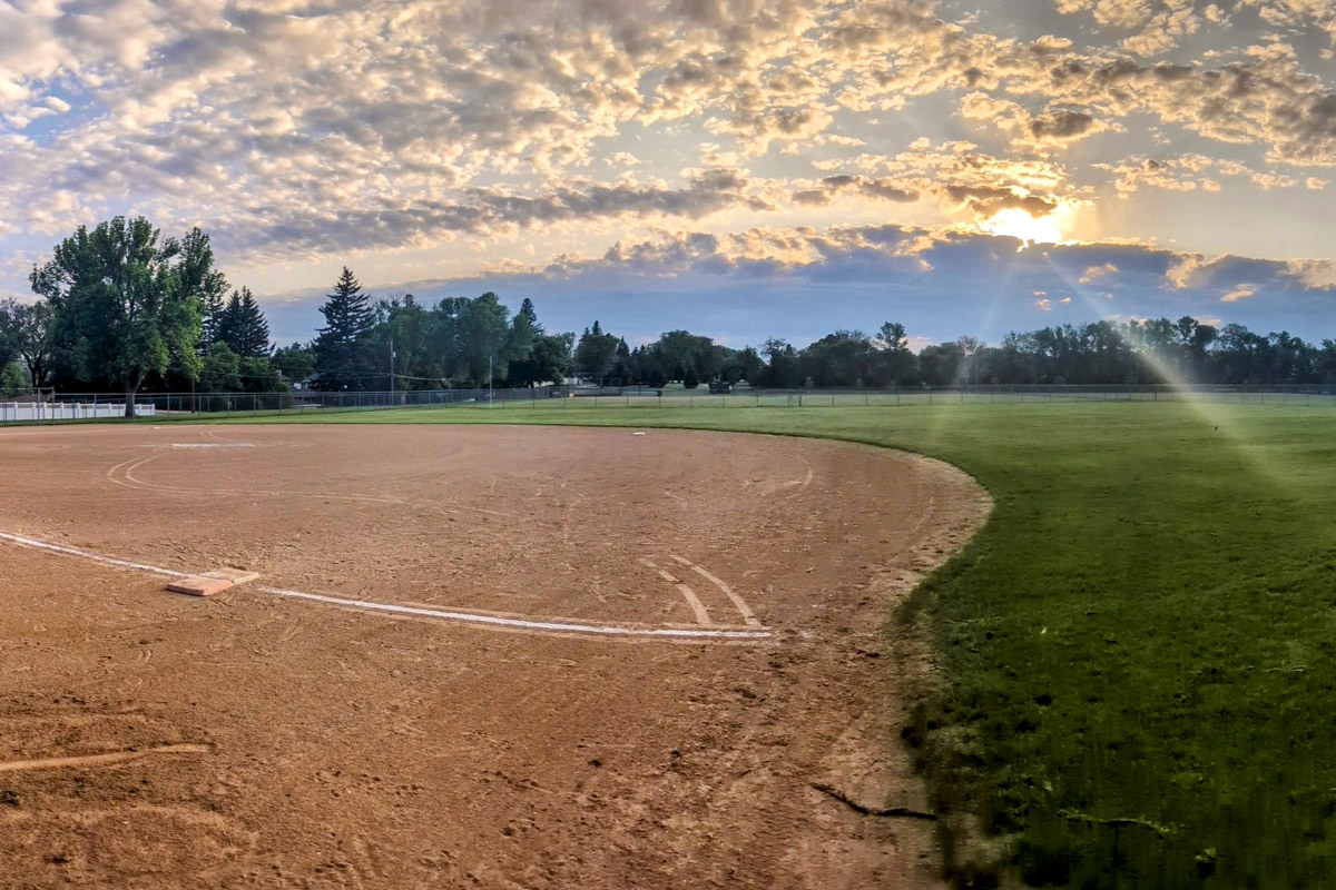 wide angle view of a softball field with the sun setting in the background