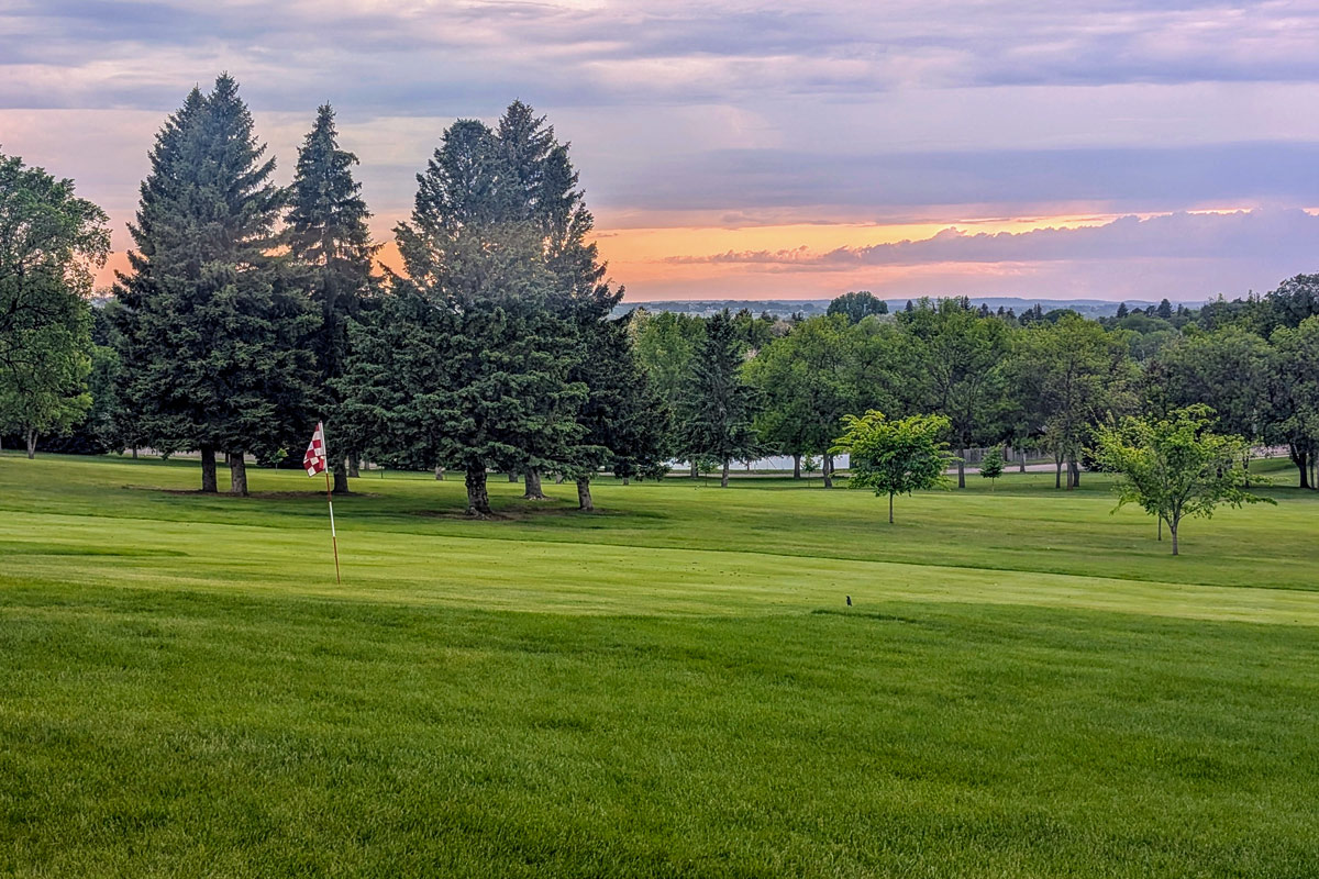 hole at golf course with sunset and trees in the background