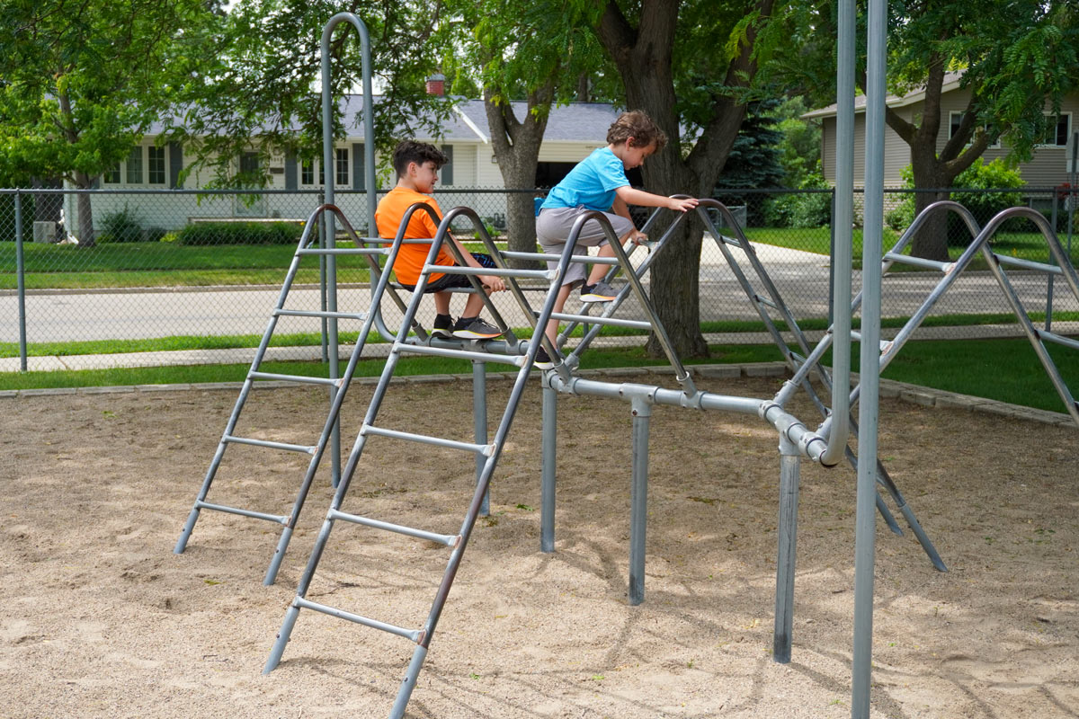 two kids playing on a jungle gym outside