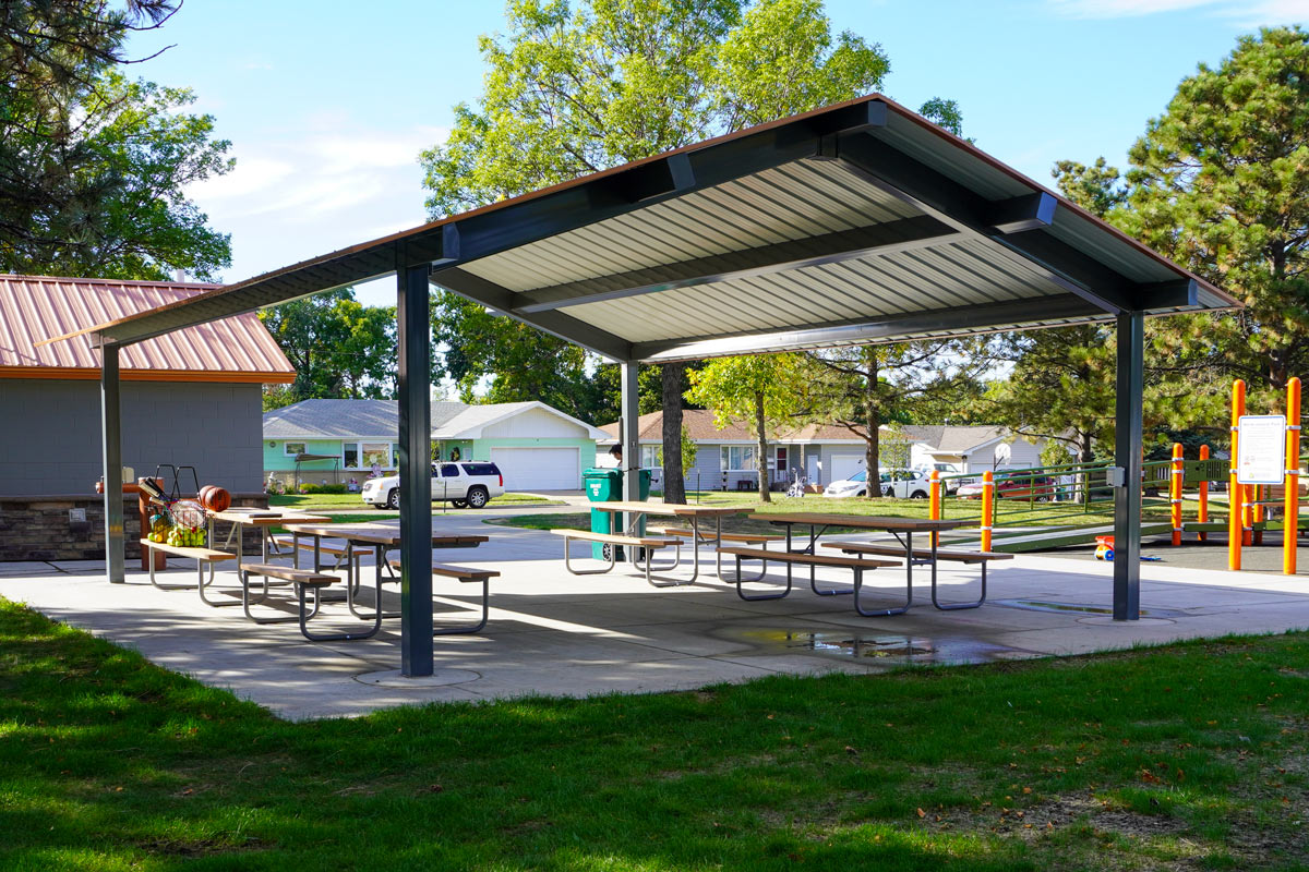 outdoor shelter with four picnic tables near a playground and bathroom