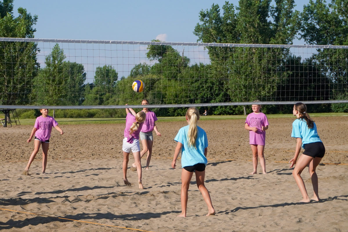5th & 6th graders playing sand volleyball, one player bumps ball in the air toward the net