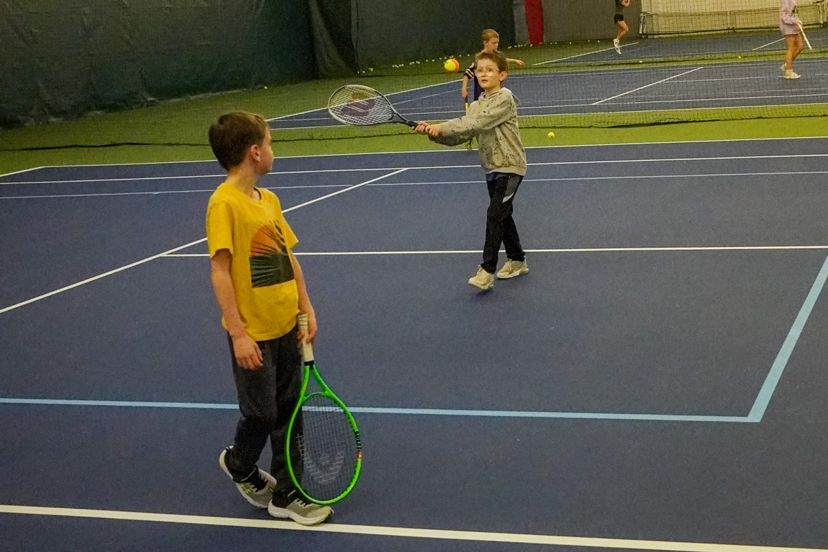 two boys playing tennis together at an indoor court